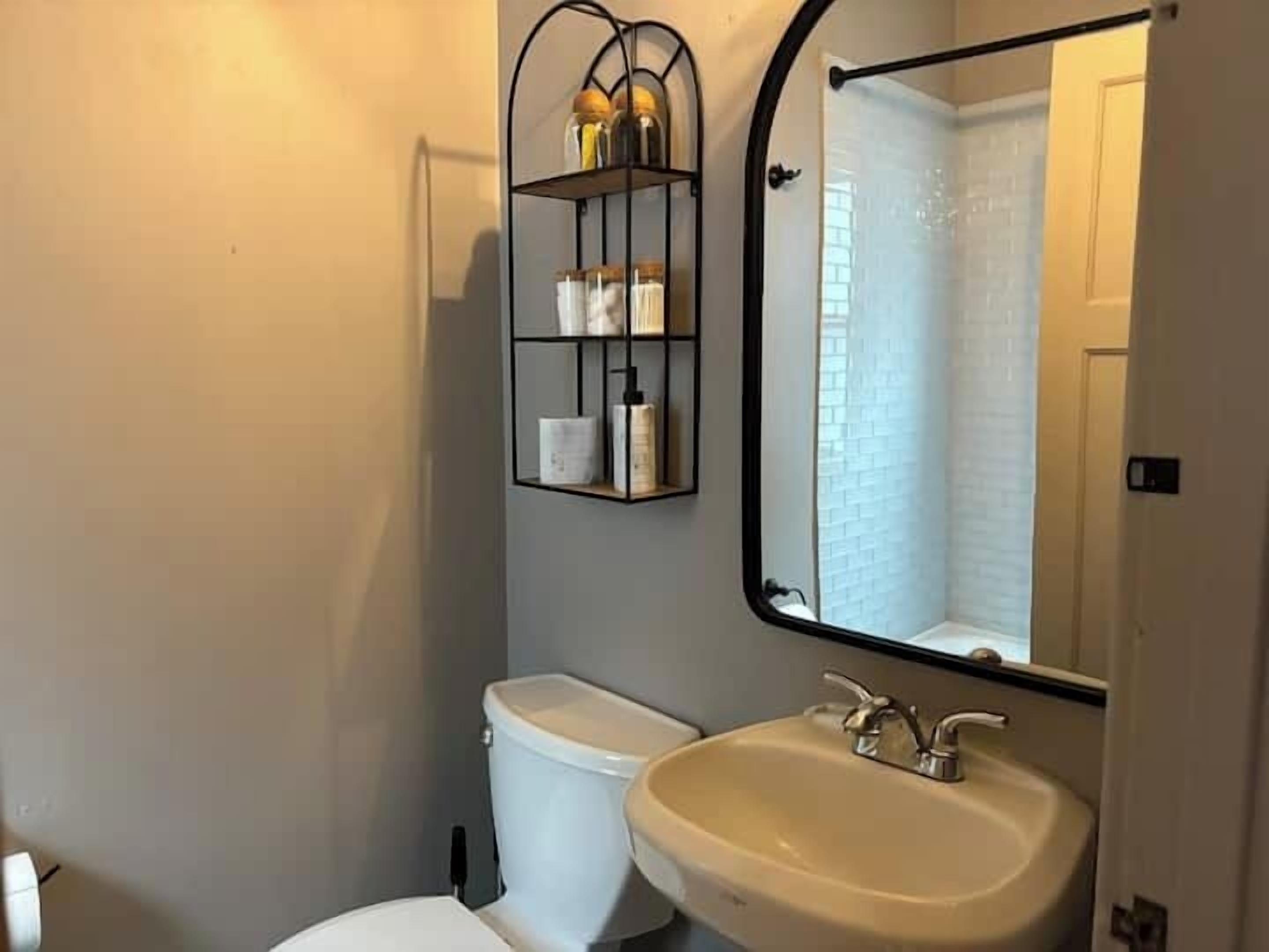 Un bagno con un water bianco, un lavandino color beige e uno scaffale in metallo nero con articoli da toilette.