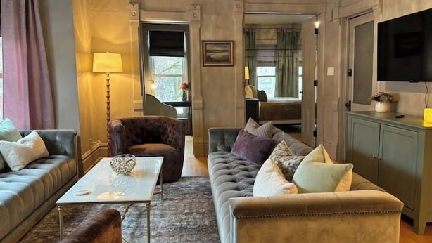 A cozy living room with a sofa, armchair, and a coffee table. There is a television on the wall and a cabinet with a flat-screen TV. - Gorgeous Brewers Hill Victorian (Milwaukee)