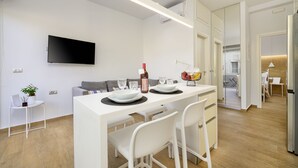 Een moderne keuken met een centraal eiland, witte stoelen, een flatscreen televisie en een zithoek met een bank en tafel.