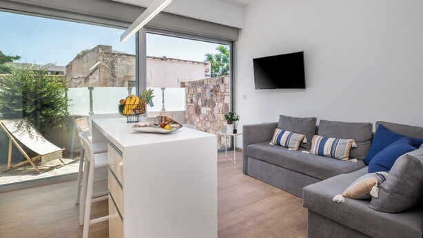 Een moderne woonkamer met een grijze bank, een wit bureau en een groot raam met uitzicht op de stad.