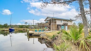 A house with a dock extending into a calm body of water, surrounded by greenery and a clear sky. - Waterfront Bay St Louis Home w/ Private Dock! (Bay St Louis)