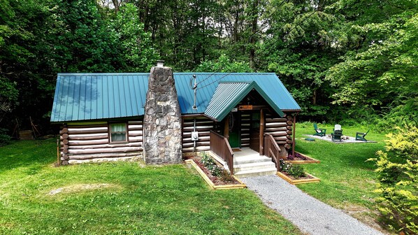 Una cabaña de troncos con chimenea de piedra, un porche y un sendero de grava que conduce a la entrada.