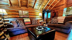 A log cabin interior with a wooden floor, two sofas, a coffee table, and a lamp. - Cozy log cabin with hot tub in Markleysburg! (Markleysburg)