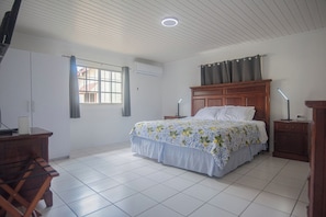 A bedroom with a bed, bedside tables, a desk, and a window with curtains. - Aruban Home Close to Beach (Oranjestad)