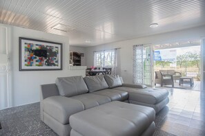 A modern living room with a sectional sofa, a dining area with a table and chairs, and a kitchen area with cabinets and a countertop. - Aruban Home Close to Beach (Oranjestad)