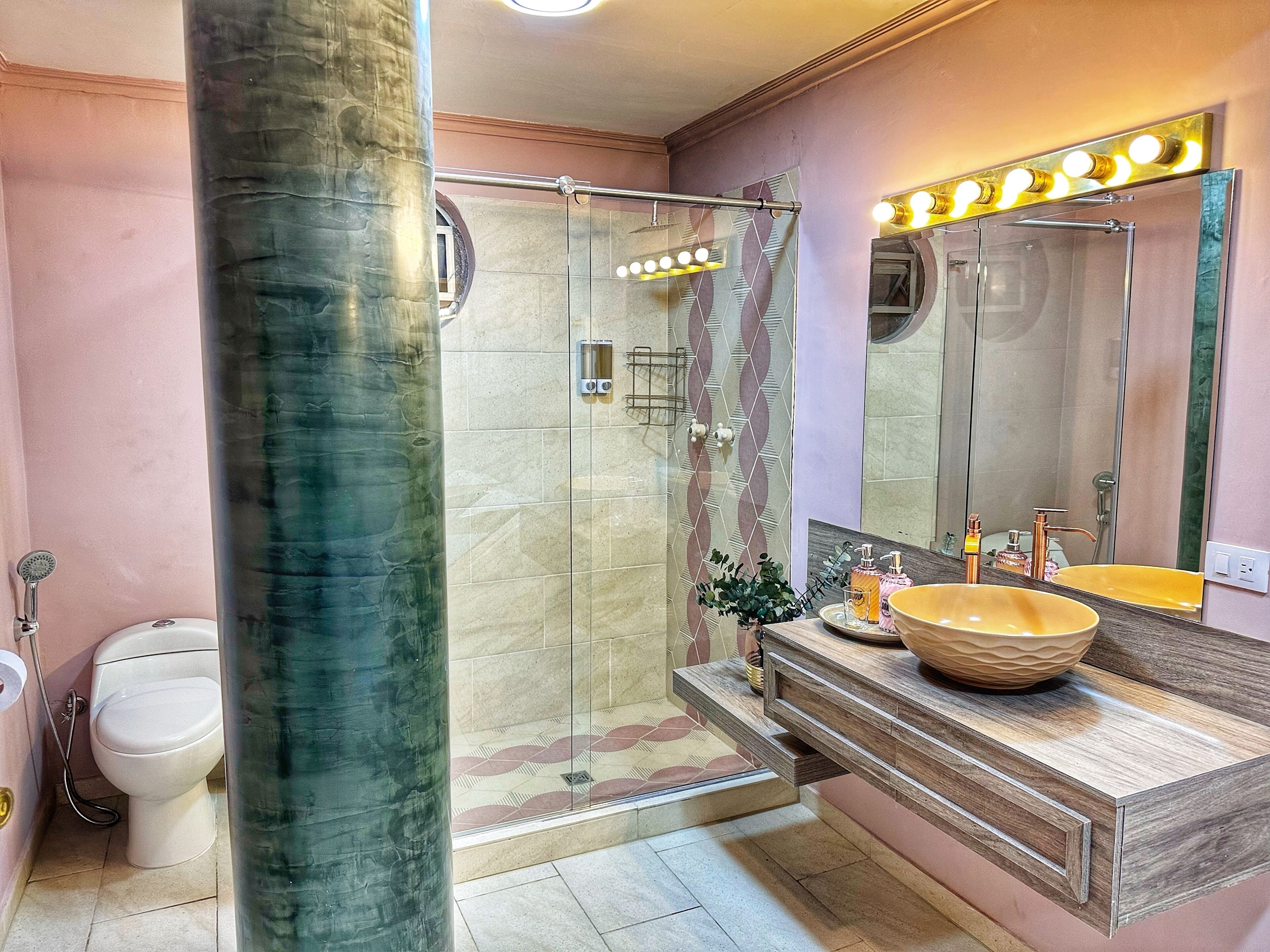 A bathroom with a glass-enclosed shower, a vanity with a large bowl sink, and a mirror with lights above it.
