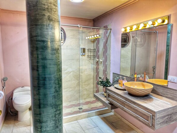 Une salle de bain dotée d’une douche à parois de verre, d’un meuble-lavabo avec un grand vasque et d’un miroir avec des lumières au-dessus.