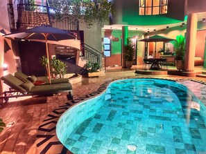 Une piscine intérieure dotée de chaises longues et de parasols, entourée d’un sol carrelé et de plantes en pot.