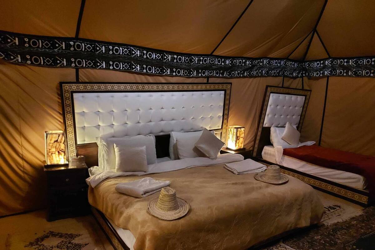 Une vaste et luxueuse pièce aménagée comme une tente, avec un grand lit, deux tables de chevet et un mur orné de motifs.
