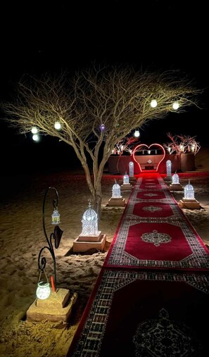 Un chemin bordé de lanternes décoratives et d’un tapis rouge menant à une structure illuminée en forme de cœur.
