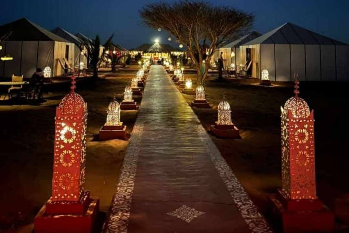 Un sentier bordé de lanternes illuminées qui mène à une rangée de tentes.
