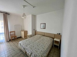 A bedroom with a bed, a chair, a desk, a hanging light, and a window with curtains.