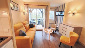 Un salon comprenant un canapé, un fauteuil, une petite table, un téléviseur et une porte-fenêtre coulissante donnant sur un espace extérieur.