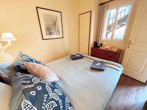 A neatly made bed with patterned bedding, a bedside table with a lamp, a framed picture on the wall, and a window with curtains.