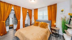 A hotel room with a large bed, orange curtains, a small round table, and a large window. - Luxury 3 Bedroom Home, Quiet Neighborhood, Pet Friendly, & Near Beaches!  (Clearwater)