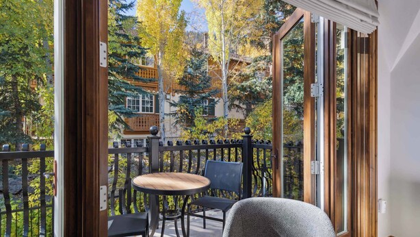A balcony with a table and chairs, a view of trees and buildings, and a wooden door. - The Aspen Mountain Residences 42ABC (Aspen)