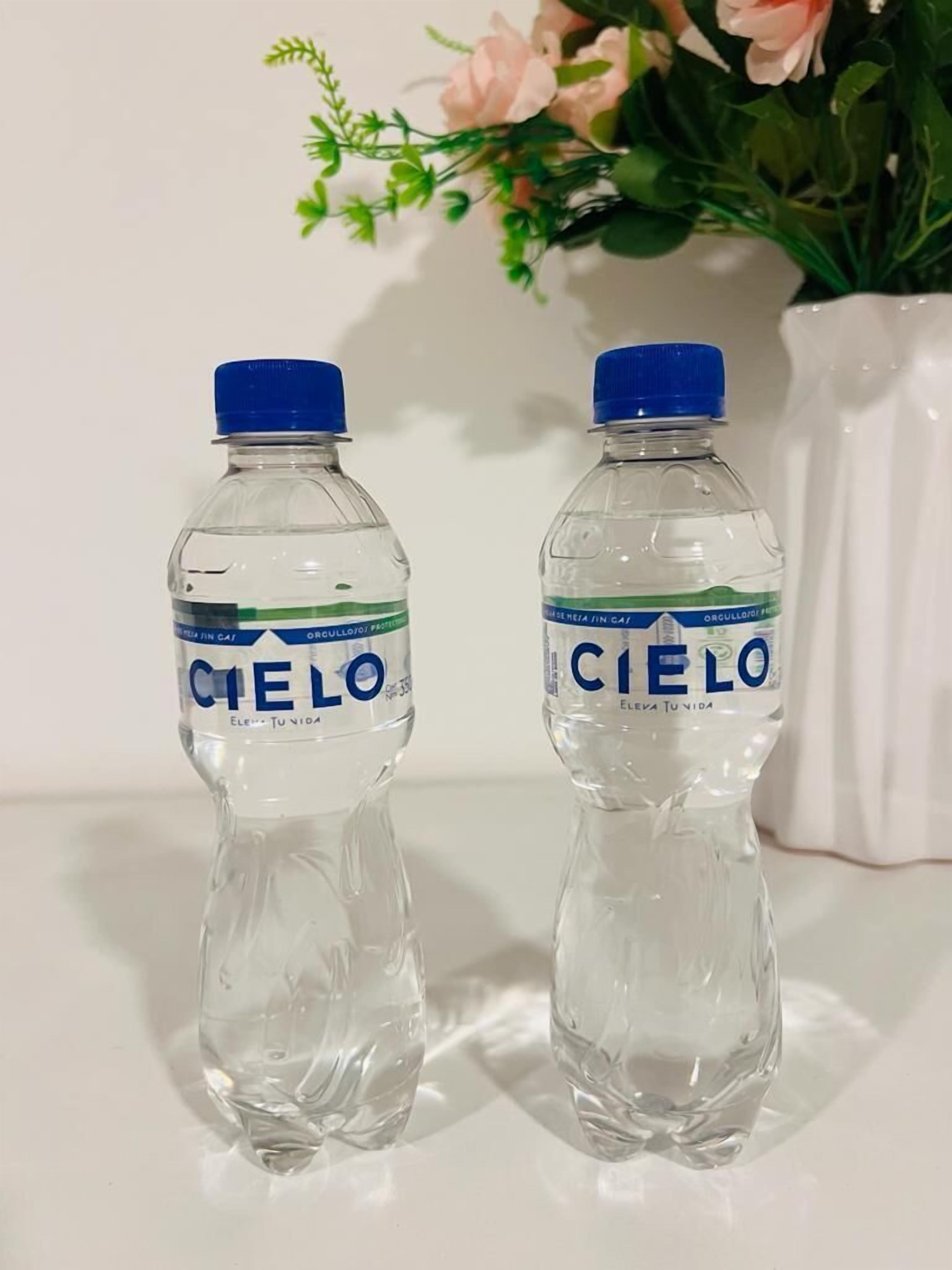 To flasker Cielo vand på en hvid overflade med en blomstervase i baggrunden.