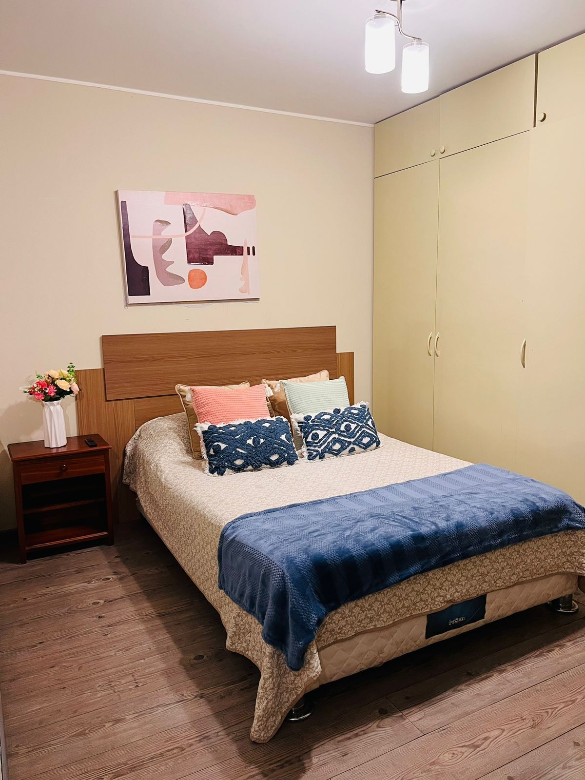 Un dormitorio con cama, mesita de noche, una obra de arte en la pared y armario.