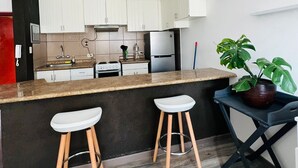 A modern kitchen with white cabinets, a granite countertop, and two bar stools. - Tezza Polo Aparts (Santiago de Surco)