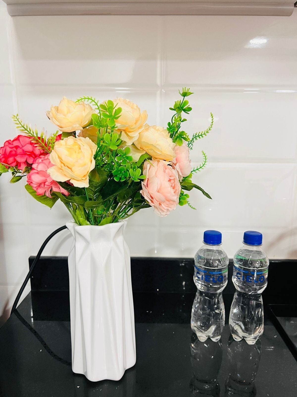 A white vase with a bouquet of flowers on a black countertop.