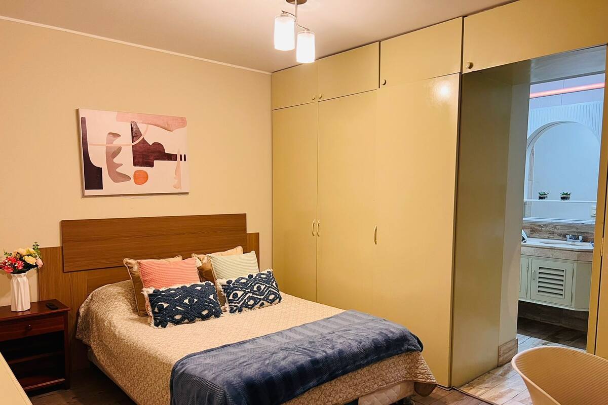 A bedroom with a bed, a nightstand, a bedside table, a mirror, and a wardrobe.