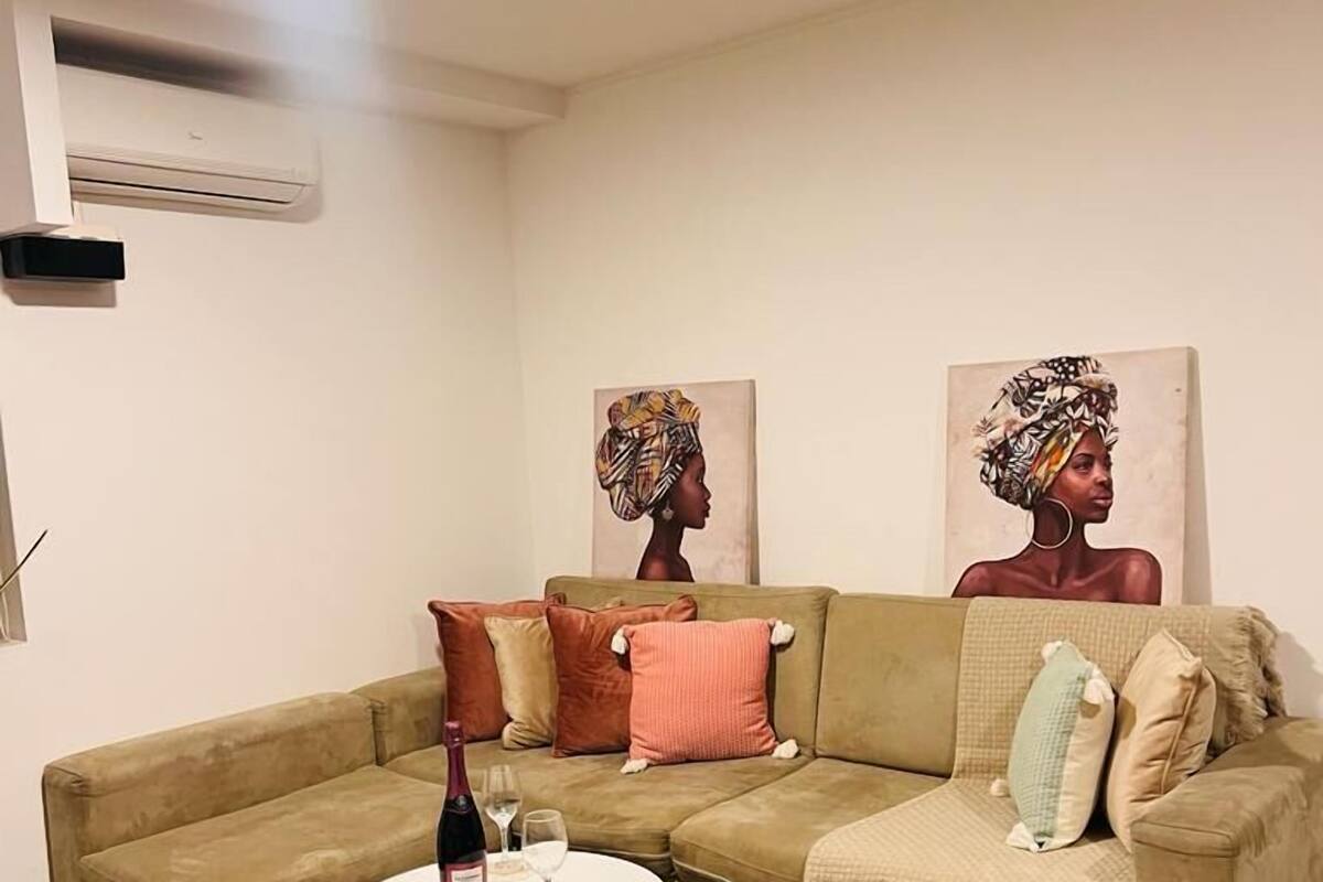A living room with a beige sectional sofa, a round coffee table, and two artworks on the wall.