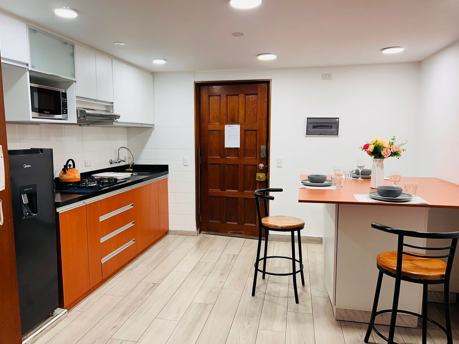 Una cucina moderna con forno a microonde, fornello e forno integrati, mobili in legno e un piccolo angolo ristoro con sgabelli.