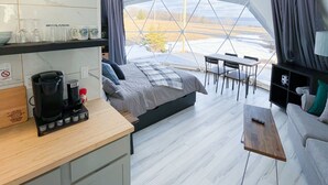 Alojamiento moderno tipo tienda con cocina, cama y zona de estar con vistas al exterior.