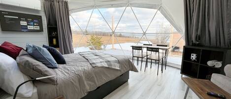 A tent-style room with a bed, a TV, a table, and a view of the outdoors.