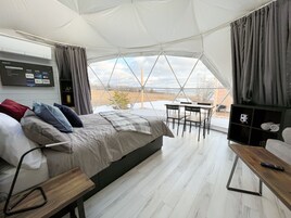 Habitación tipo tienda de campaña con cama, televisor, mesa y vistas al exterior.