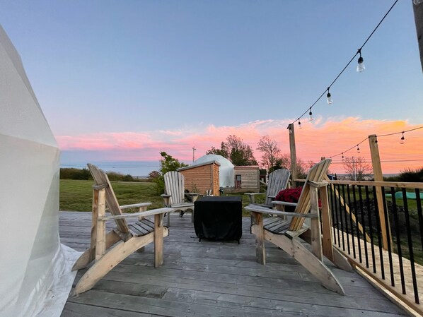 A wooden deck with two Adirondack chairs, a small shed, and a string of lights against a sunset sky.