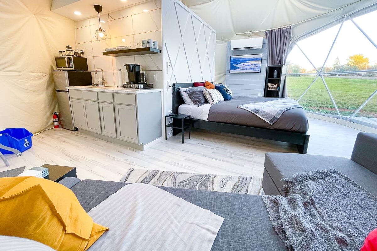 Alojamento moderno estilo tenda, com cozinha compacta, cama com várias almofadas e vista para o exterior.