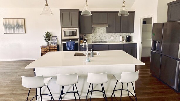 A modern kitchen with a central island, bar stools, stainless steel appliances, and pendant lighting. - House in North Fort Worth (Haslet)