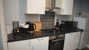 Una cocina moderna con armarios blancos, encimera negra, cafetera, tostadora y dispensador de agua.
