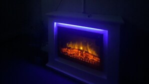 Un televisor de pantalla plana montado en la pared mostrando el logotipo de Netflix. Debajo del televisor, hay una chimenea con un marco de luz LED azul.