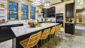 A modern kitchen with a large island, black cabinets, and a marble countertop. - Creekside Family Lodge with Luxury Touches (Hochatown)
