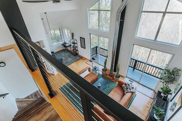 A spacious living area with a staircase, large windows, and a balcony.