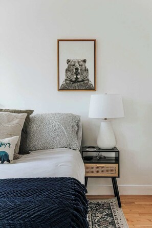 A bedroom with a bed, pillows, a bedside table with a lamp, and a framed picture on the wall.