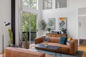A modern living room with a leather sofa, a coffee table, and a large window overlooking a balcony.