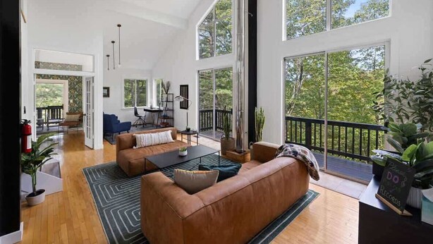 Ein geräumiges Wohnzimmer mit großem Fenster, einem braunen Ledersofa, einem Couchtisch und Blick ins Freie.