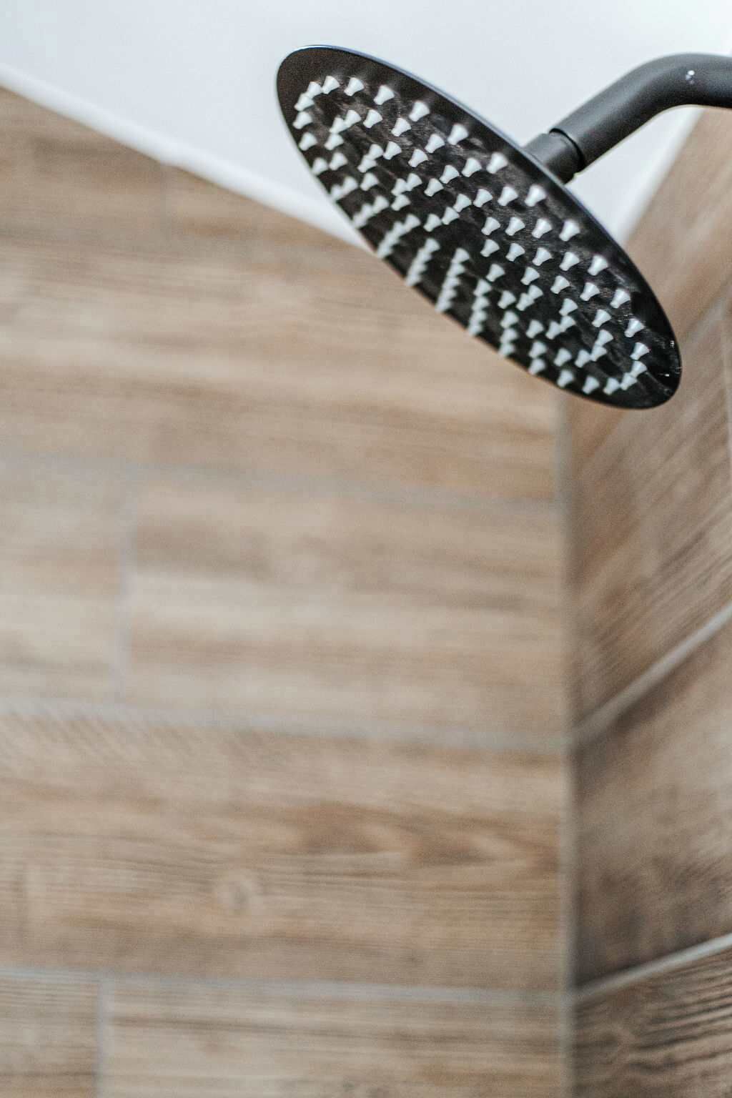 A showerhead with a black handle and white bristles, mounted on a wall with wooden paneling.