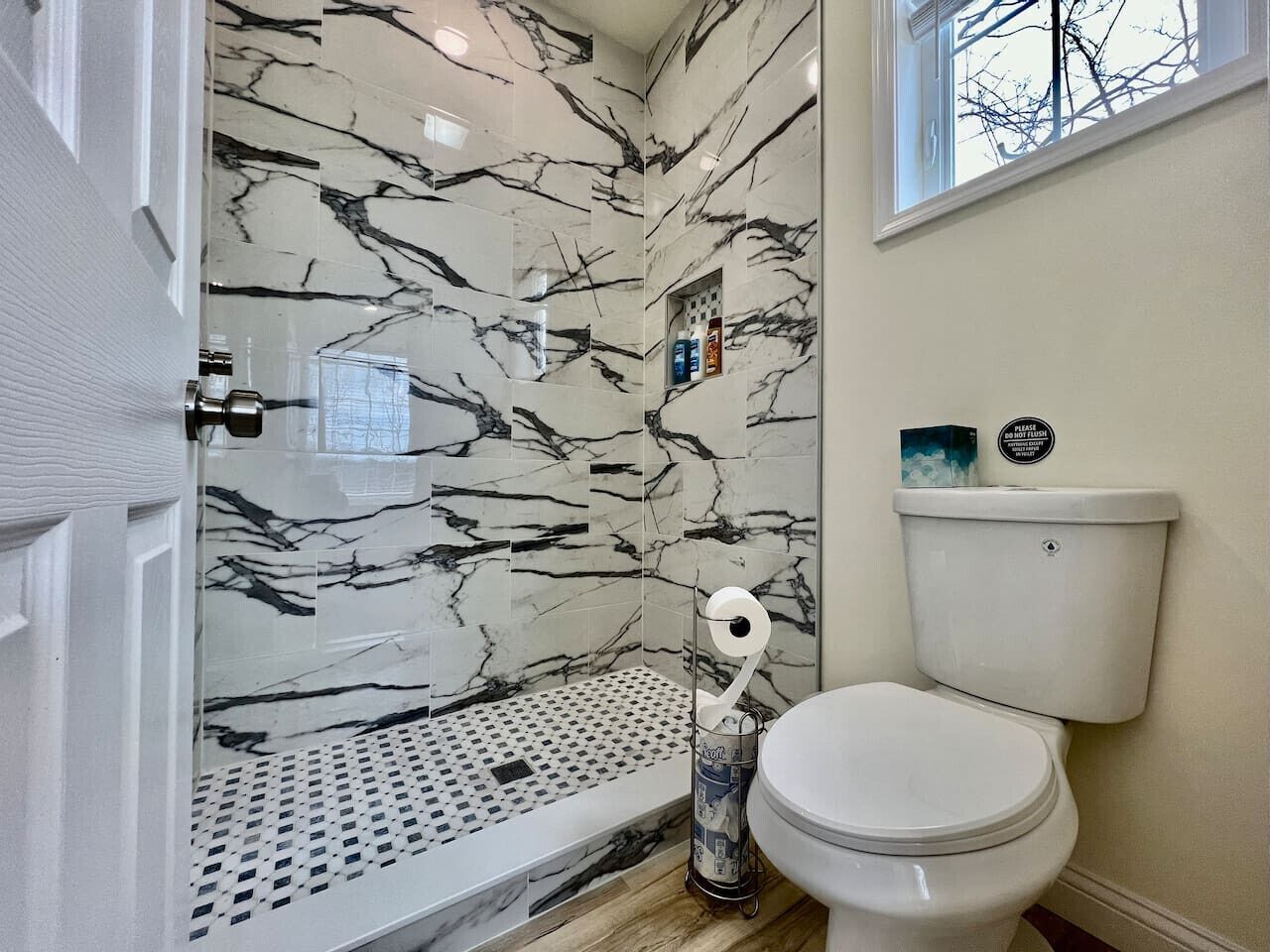 Een badkamer met toilet, een douche met marmeren wand en een raam.