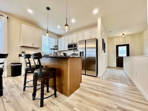 A modern kitchen with a central island, stainless steel appliances, and wooden flooring. - Beautiful NEW Ranch Home with a large deck & games (West Chester Township)