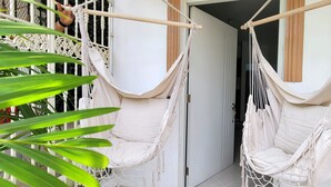 Deux hamacs blancs sont suspendus à une poutre en bois, avec une porte blanche et une plante au premier plan.