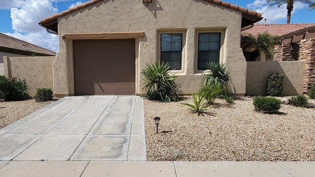 A single-story house with a garage, a small porch, and a landscaped front yard with desert plants.