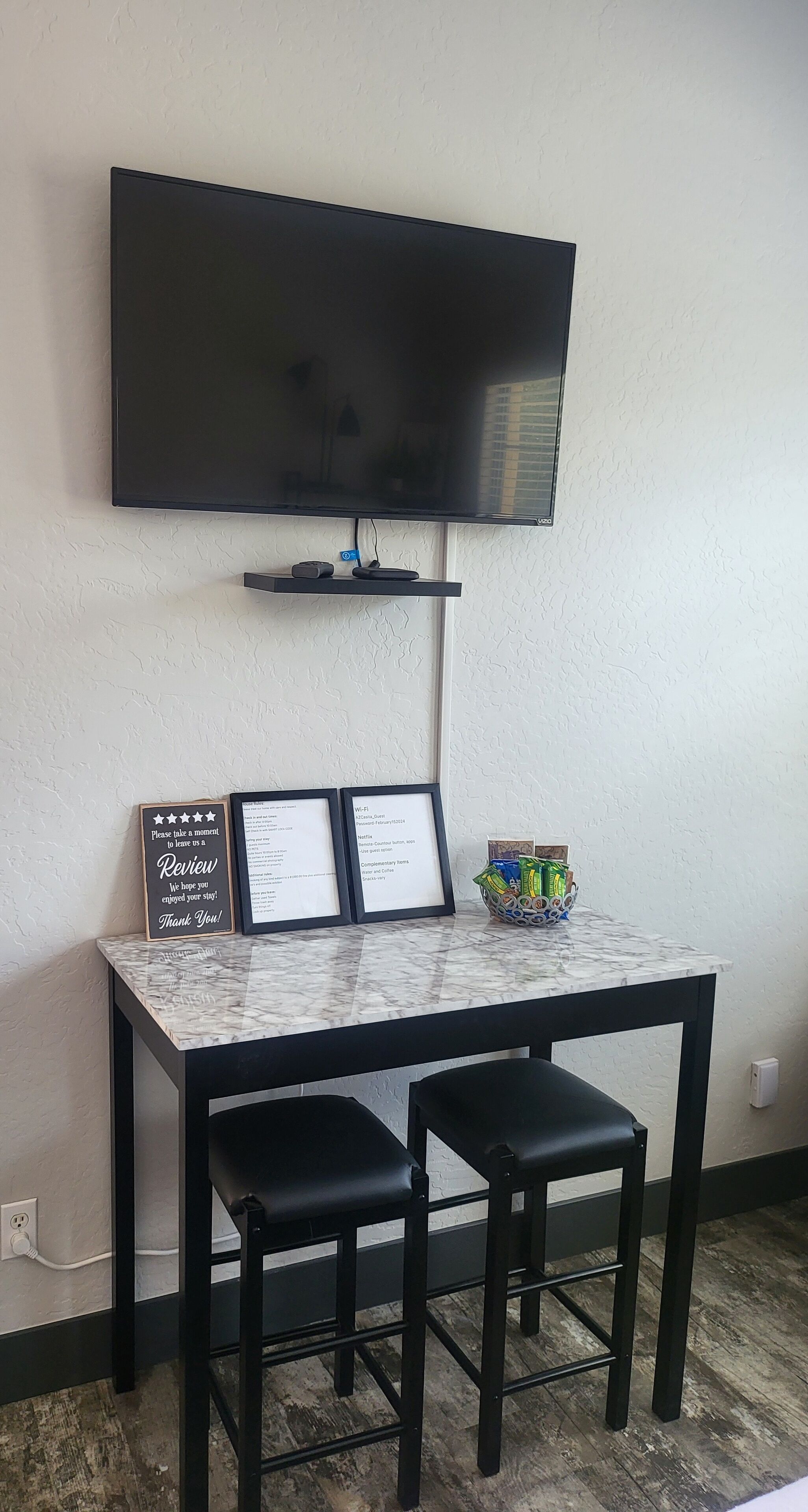A small room with a TV mounted on the wall, a table with two stools, and a sign on the wall.