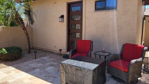 A patio with two wicker chairs and a table, a door, and a small window.