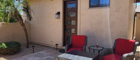 A patio with two wicker chairs and a table, a door, and a small window.