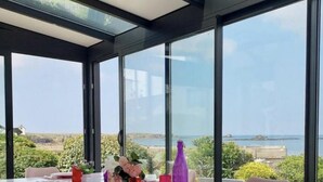 A dining area with a table set for six, large windows offering a view of the sea and landscape, and modern chairs. - Villa Cocooning Les Pieds Dans l eau (Saint-Pierre-Quiberon)