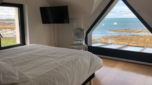 A bedroom with a bed, a toilet, a TV, and a large window with a view of the sea and boats. - Villa Cocooning Les Pieds Dans l eau (Saint-Pierre-Quiberon)
